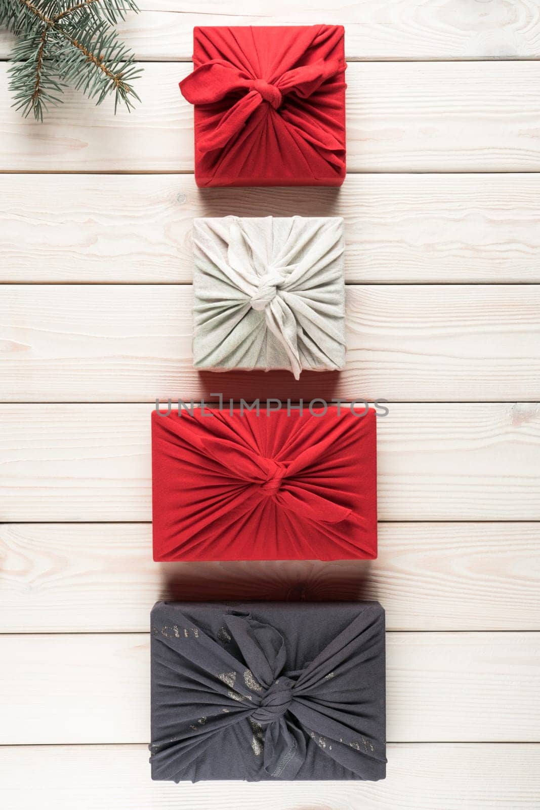 Group of christmas presents in furoshiki package, top view. Spruce branch and gift boxes on white planking. Objects layout in ascending size. Christmas or New Year holiday, eco decor, zero waste.