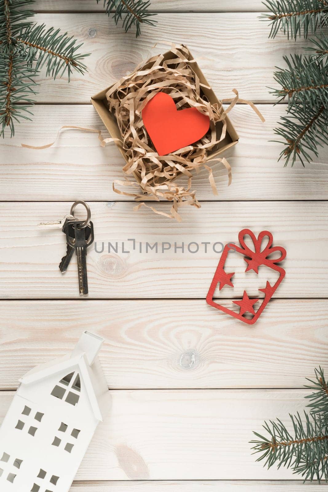Mini model of house, keys and present box with red paper heart postcard, top view. Frame from decorative spruce branches. Buying new real estate. Accommodation as gift. Christmas or New Year holiday.