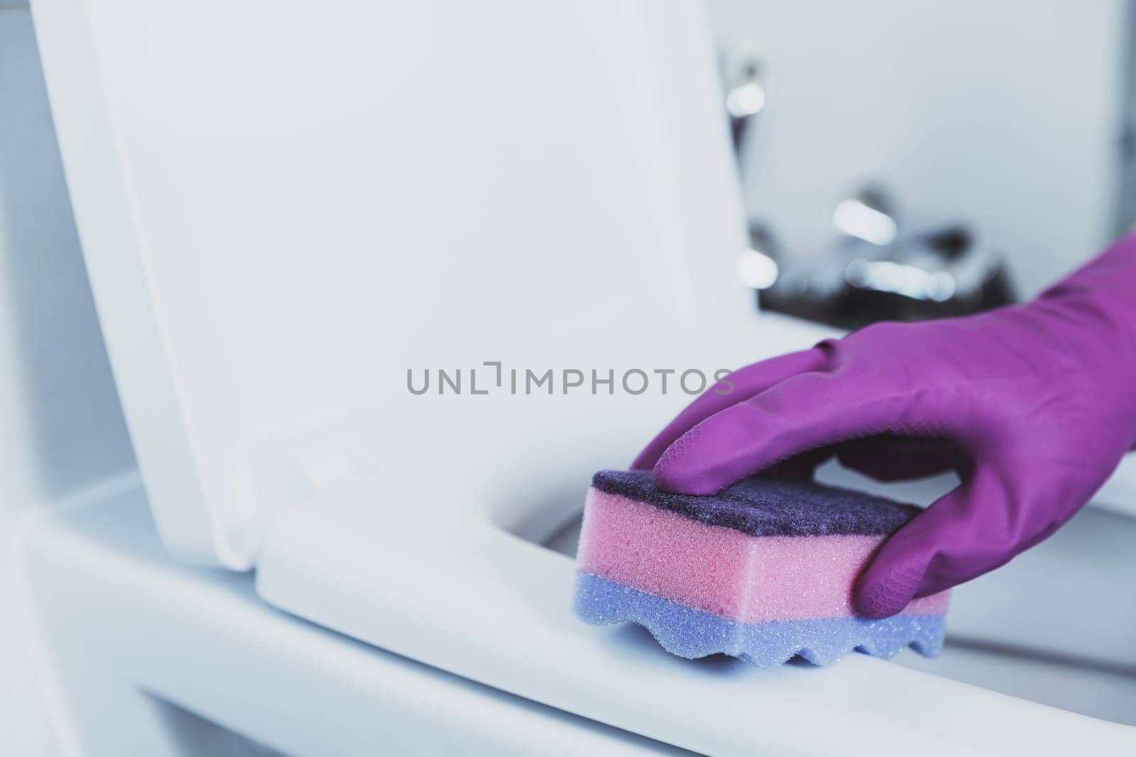 Close up on woman hand gloved in blue rubber protective gloves. Housewife cleaning toilet bowl, seat with detergent liquid, wet wipe in bathroom, restroom. Female washing, disinfecting toilet seat
