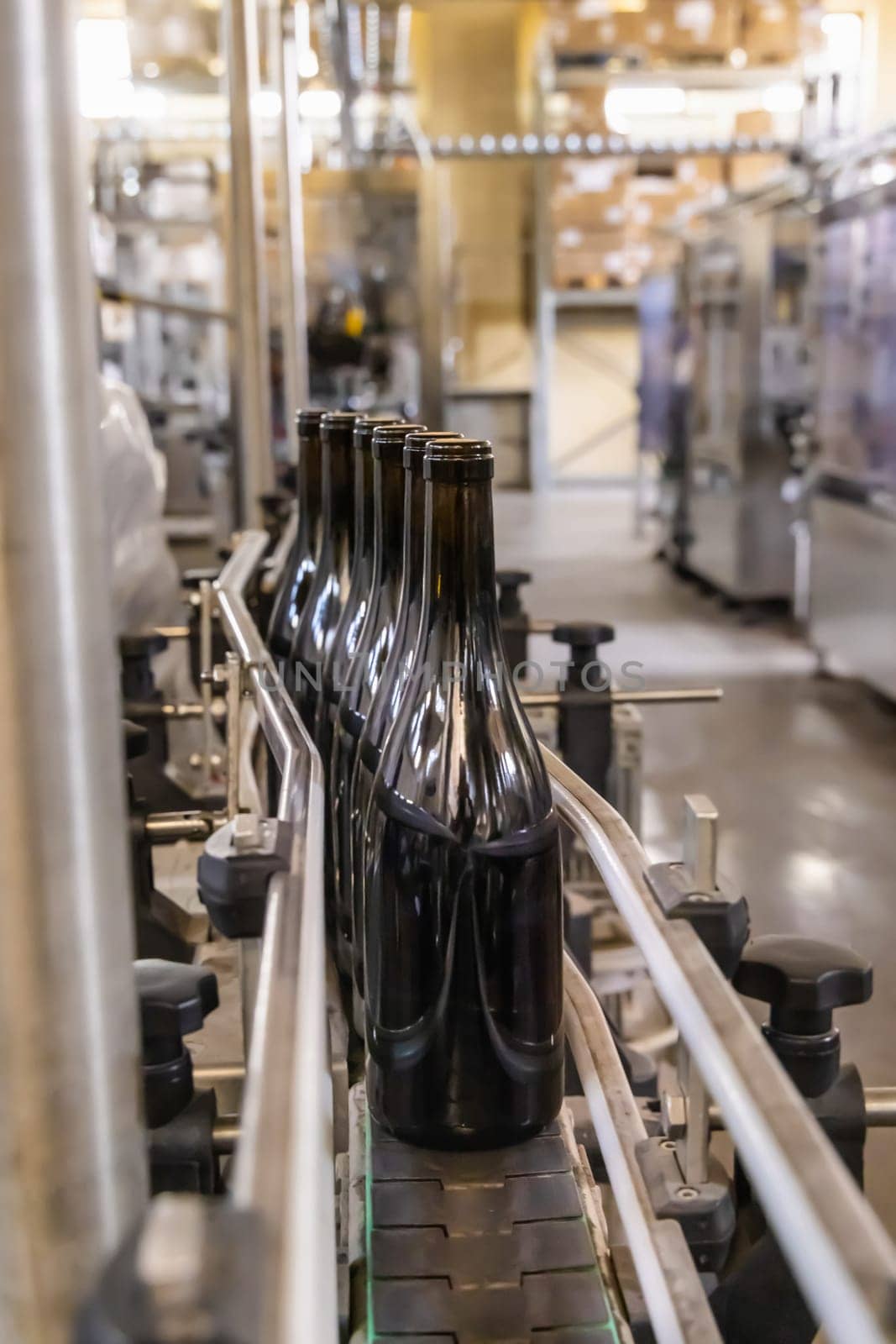 Dark glass bottles being filled with wine by industrial bottling machine at modern wine factory in Italy. Automatic conveyor line for wine-producing
