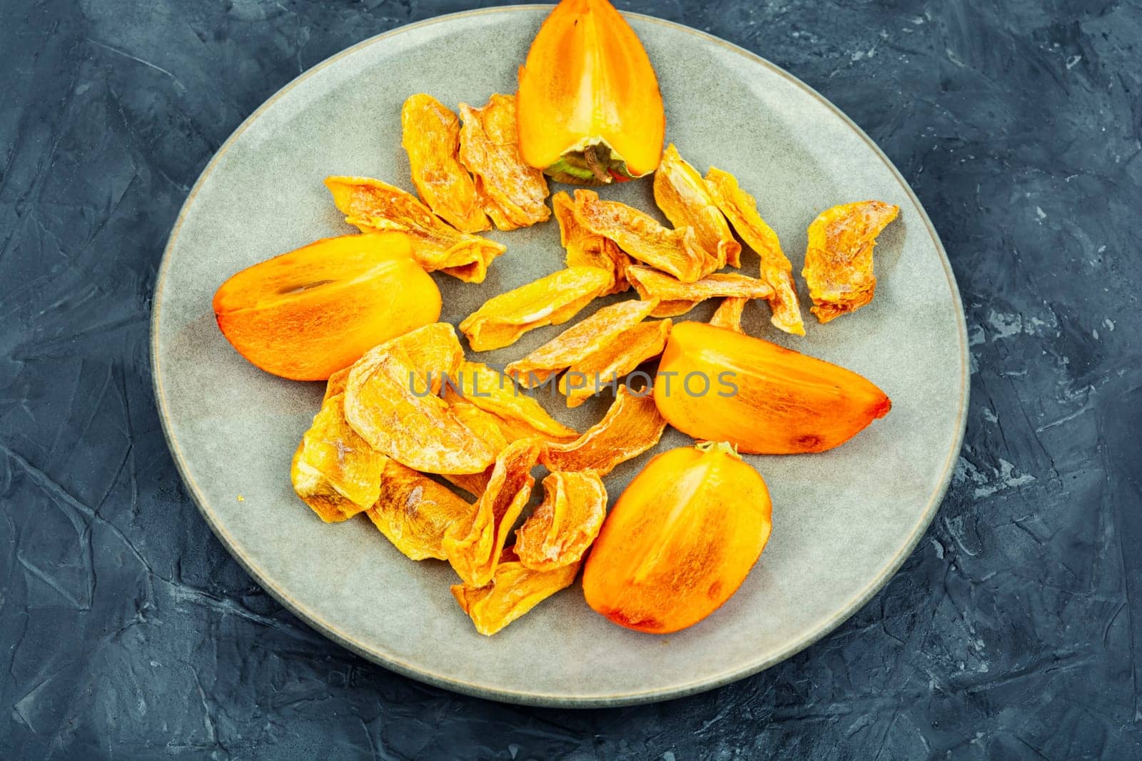 Sweet dried persimmon on the plate. Healthy vegan snacks. Copy space