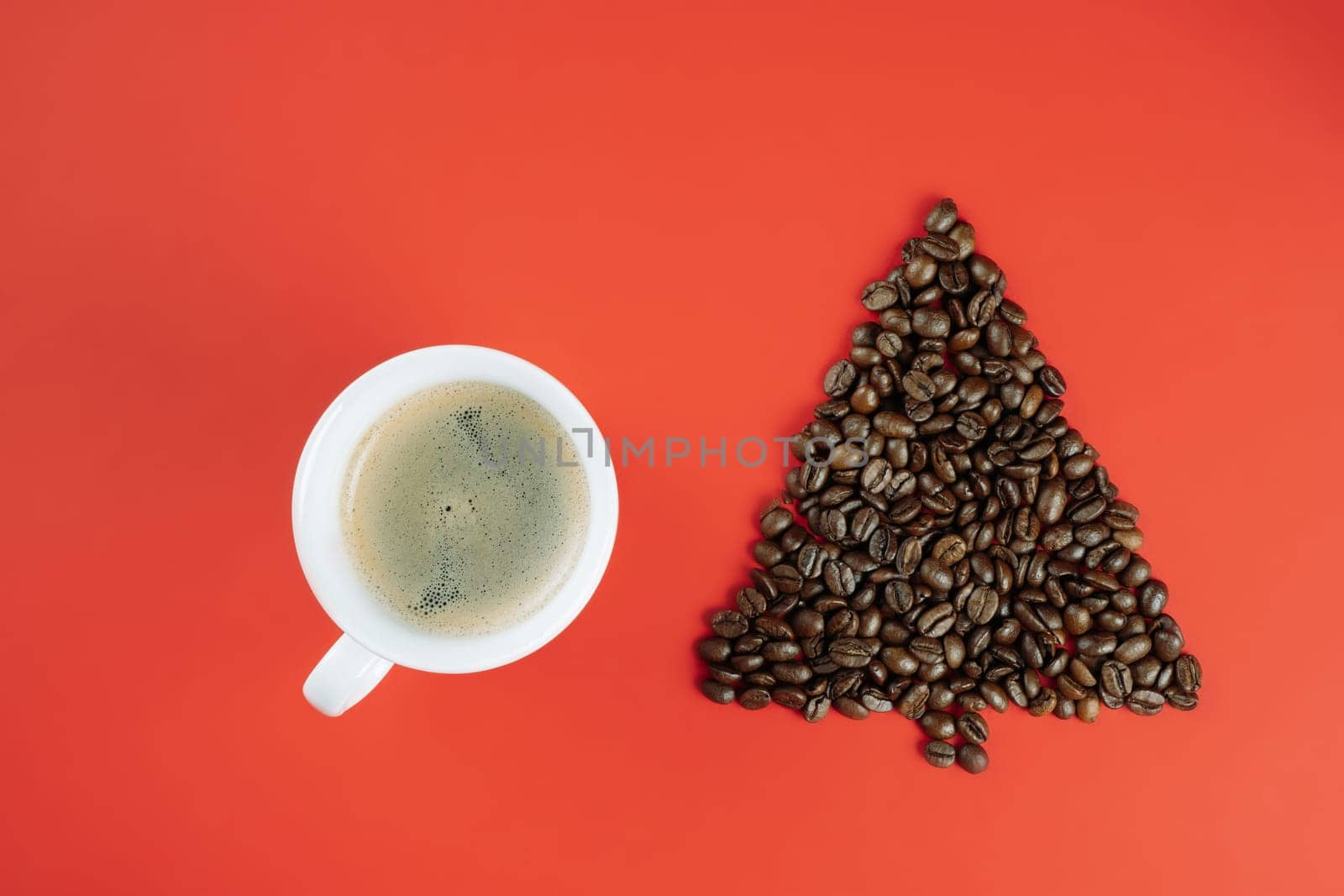 Brown coffee beans laid out in shape of Christmas tree with cup of coffee on red background. Flat lay. Copy space