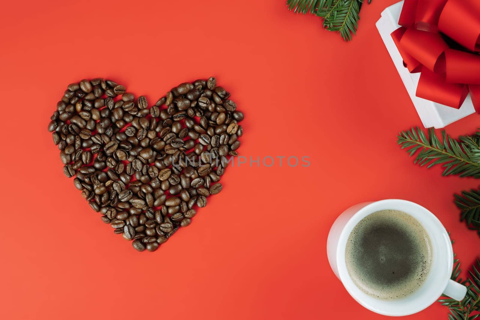 Brown coffee beans laid out in shape of heart with Christmas tree branches, cup of coffee and gift box on red background. Flat lay