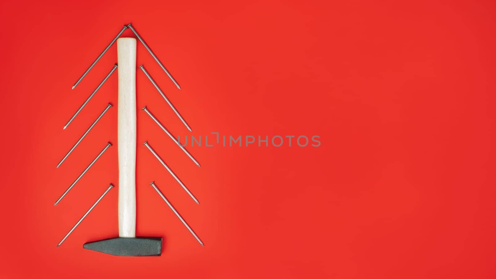 Long nails and hammer, laid out in shape of Christmas tree on red background. Banner. Flat lay. Copy space