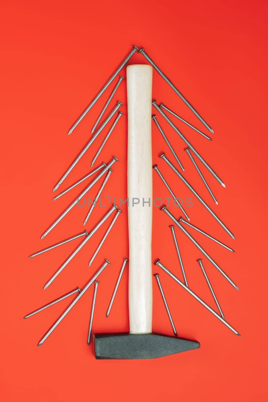 Long nails and hammer, laid out in shape of Christmas tree on red background. Vertical, flat lay