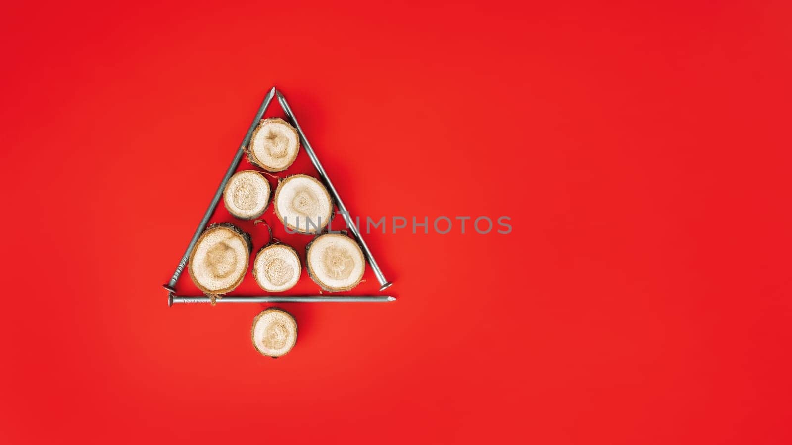 Long nails and wood cuts or branch slabs, laid out in shape of Christmas tree on red background. Banner. Flat lay. Copy space