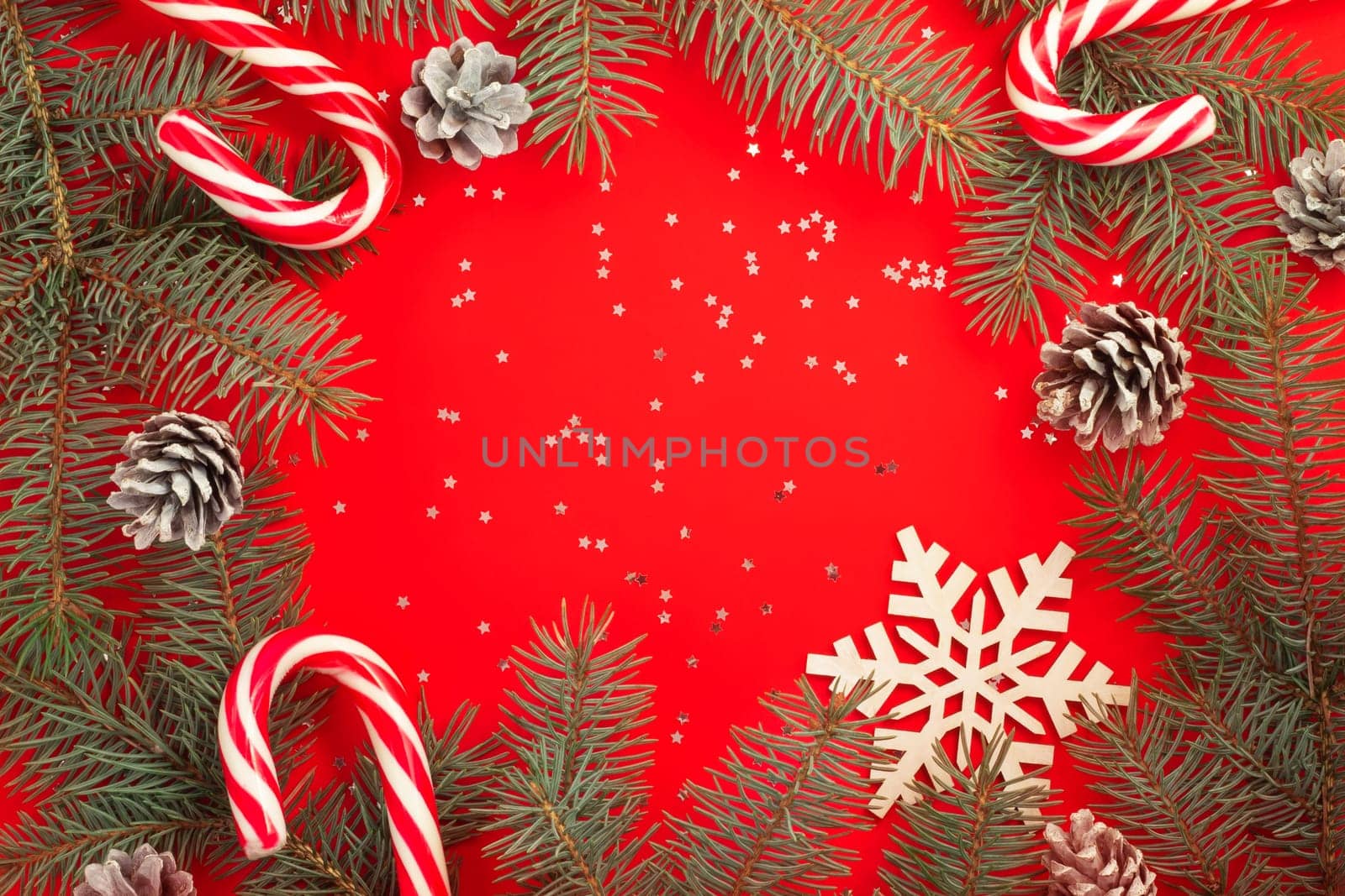 Christmas tree branches, candy canes, snowflake and pine cones on a red background with silver confetti stars. Merry christmas and happy new year concept. Flat lay. Copy space.
