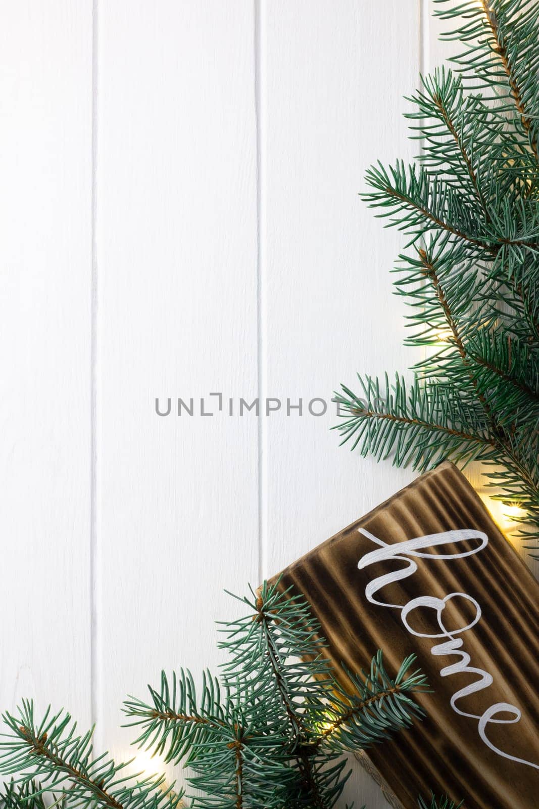 Home lettering burnt wood sign and Christmas tree branches on white wooden surface. Flat lay, copy space. Vertical