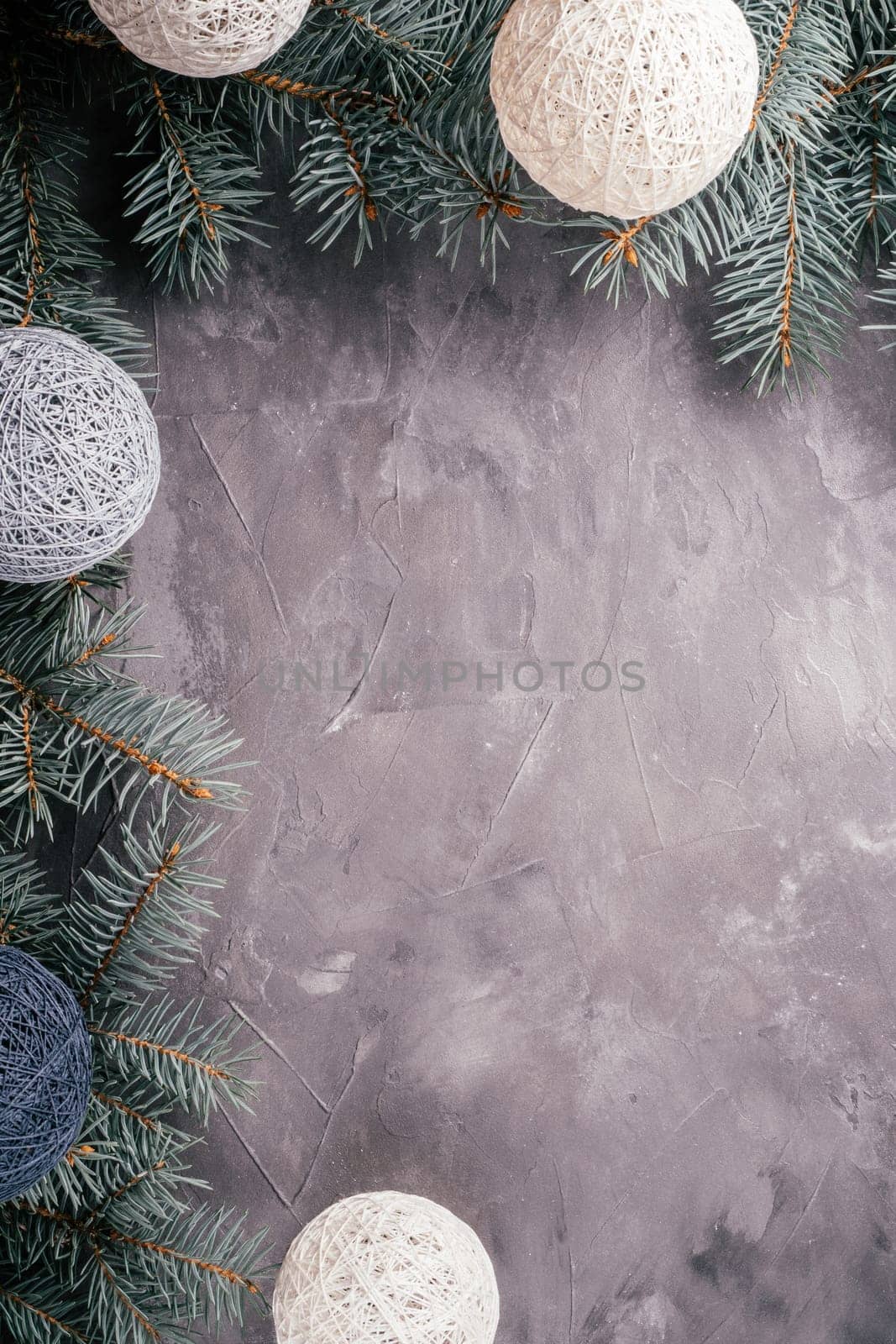 Background image of gray uneven concrete surface with Christmas tree branches and garland of balls. Top view, copy space. Vertical