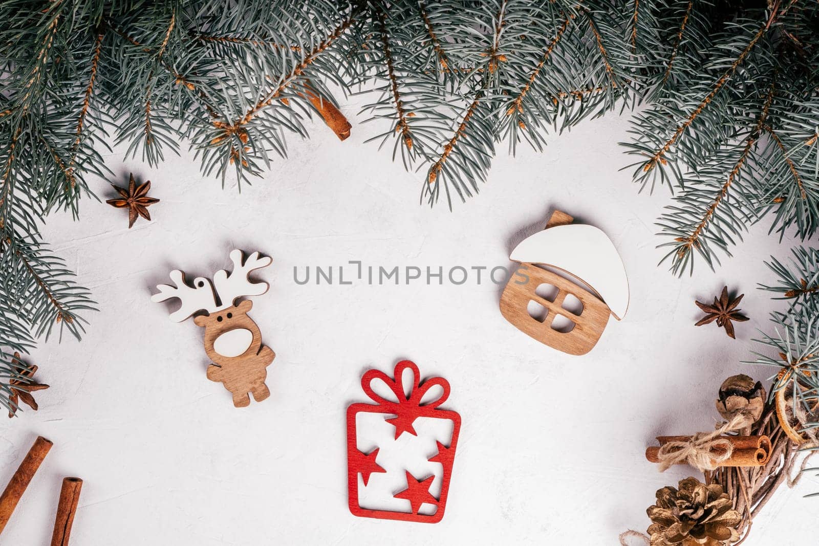 White uneven concrete surface with Christmas tree branches, cinnamon, anise and wooden decorations House, Elk, Gift. Top view.