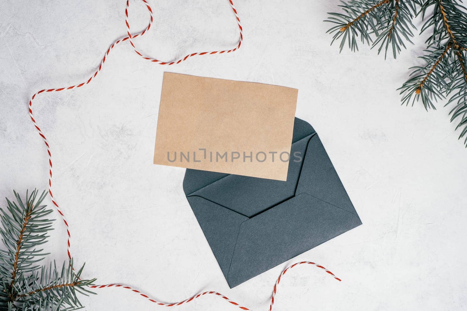 Green open envelope on white concrete background with blank kraft paper greeting card with branches of Christmas tree. New year envelope with untied cord. Copy space. Top view