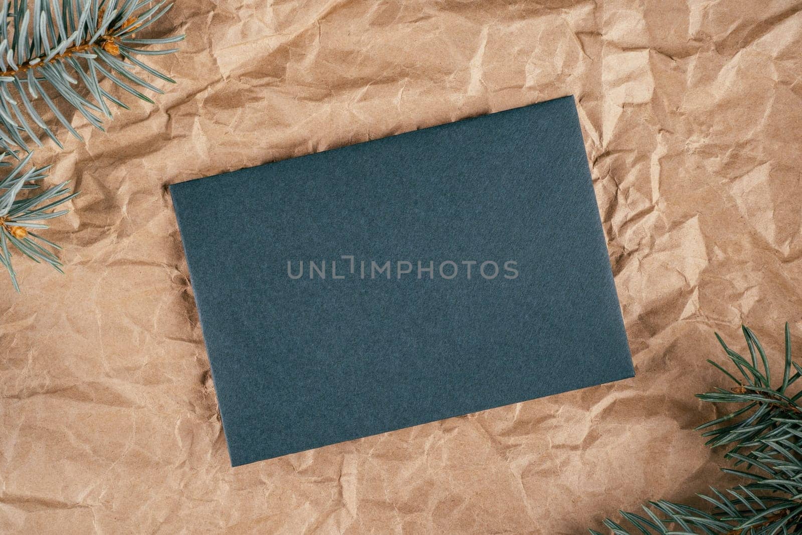 Background image of rough crumpled recycled textured kraft paper with Christmas tree branches and sheet of dark green cardboard. Top view. Copy space