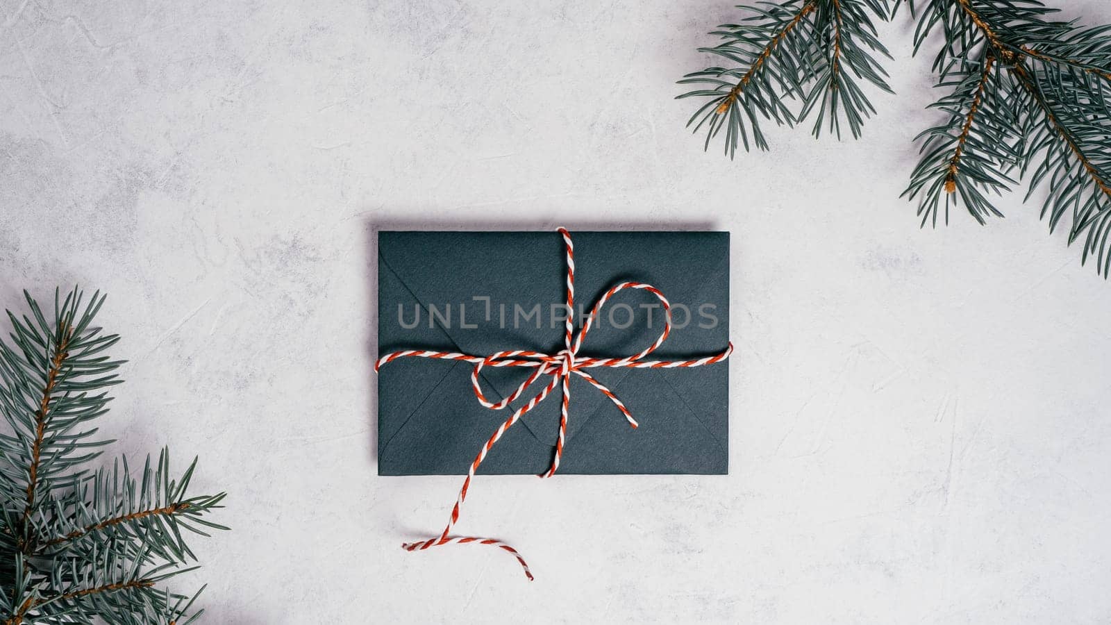Green envelope on white concrete background with branches of Christmas tree. New year envelope tied with cord with bow. Top view