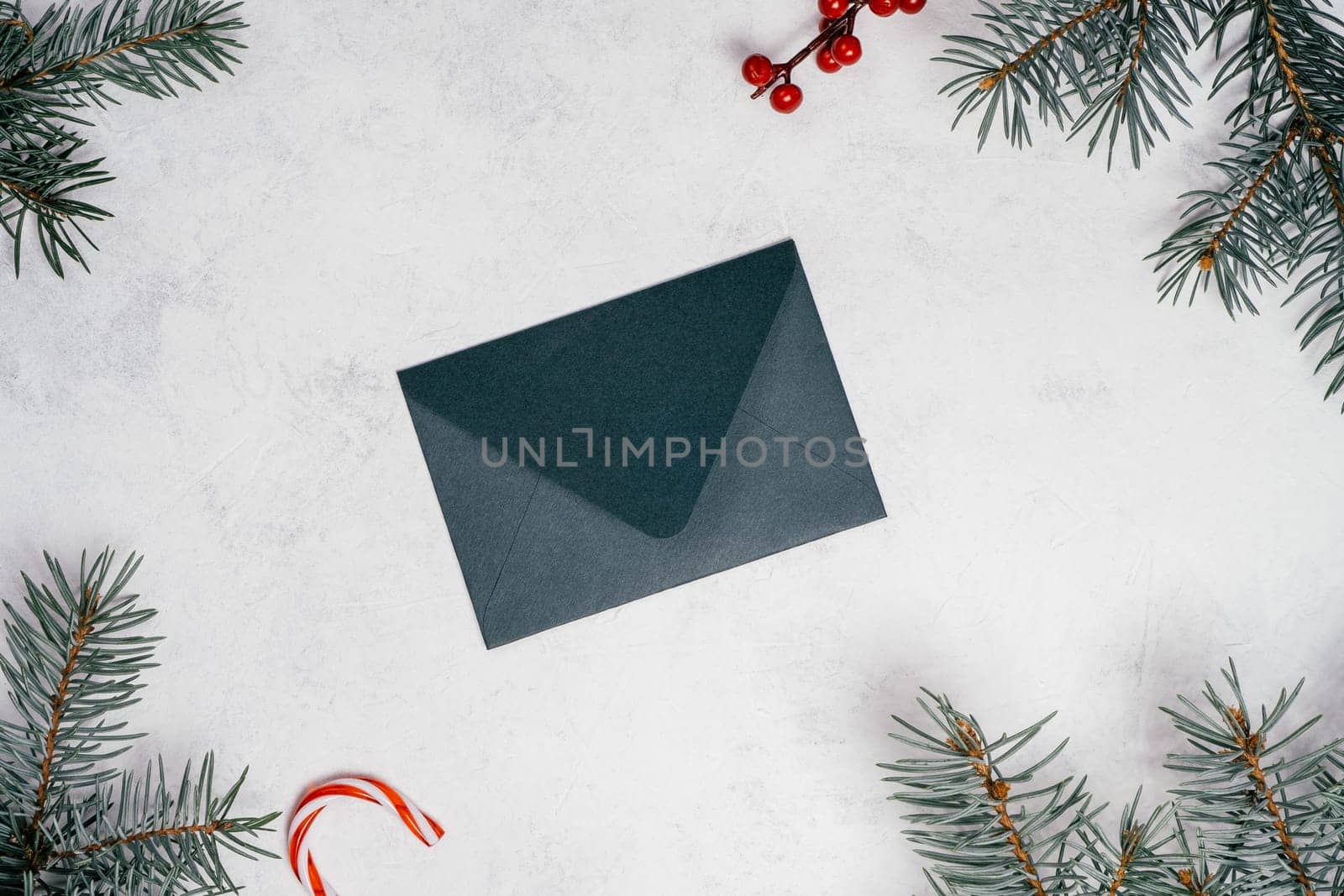 Green envelope on white concrete background with branches of Christmas tree. New year envelope. Top view