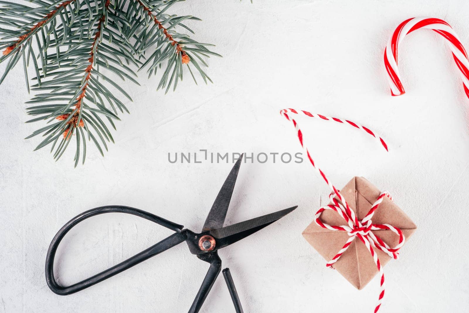Christmas gift box and lollipop, cord, scissors on white concrete background with branch of Christmas tree. Merry Christmas and Happy New Year. Top view