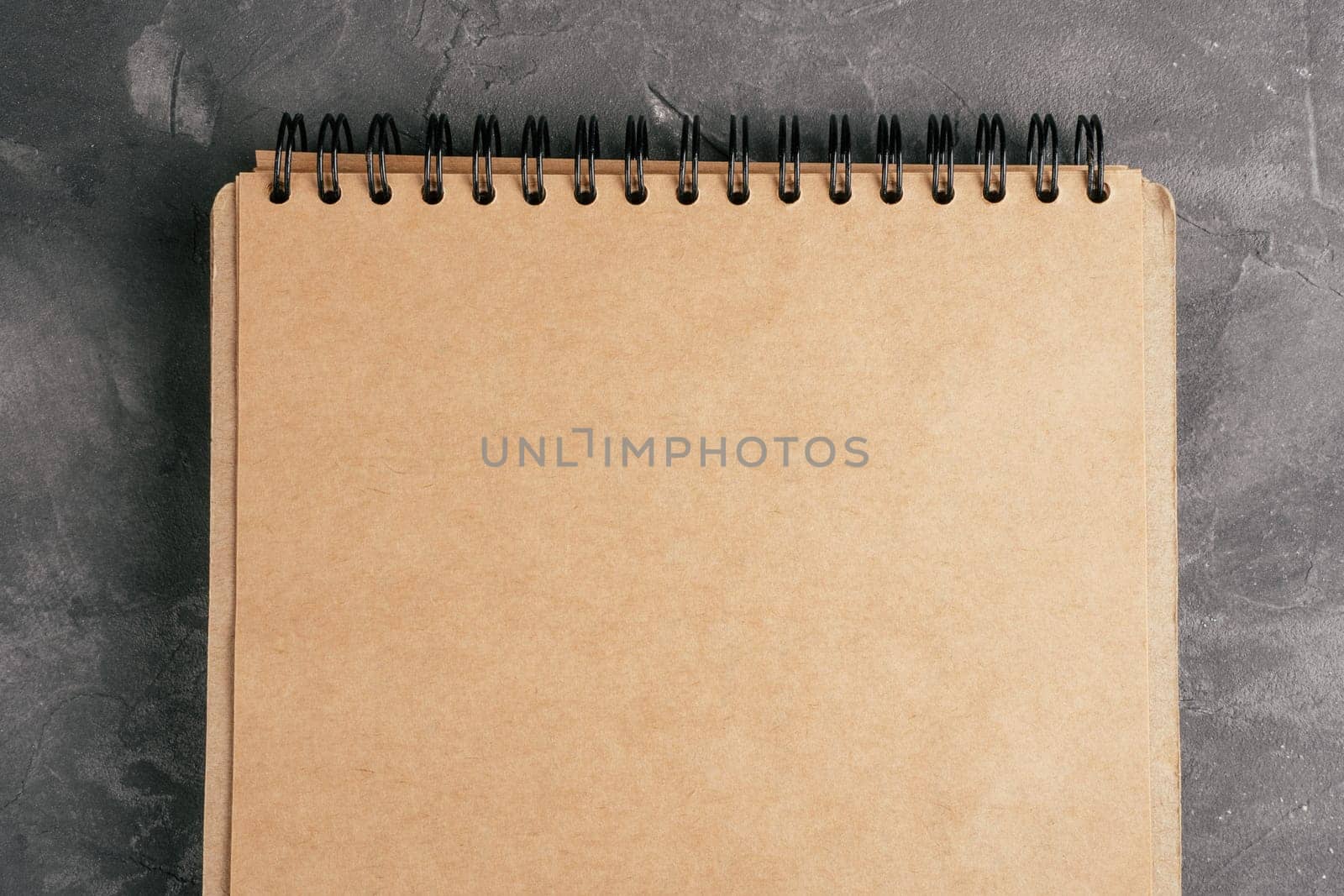 Opened brown kraft paper notebook on spring on gray concrete surface. Top view. Copy space