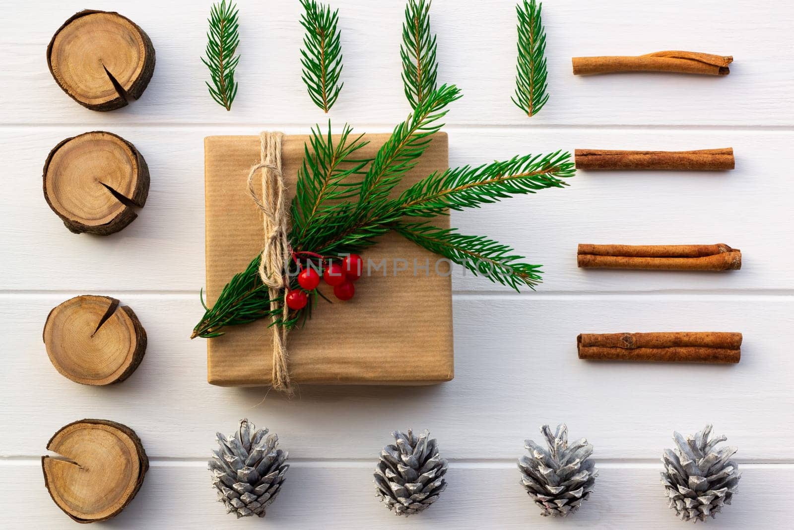Gift with green branches of a Christmas tree, red berries, cones, cinnamon sticks on a background of white boards. Flat lay.