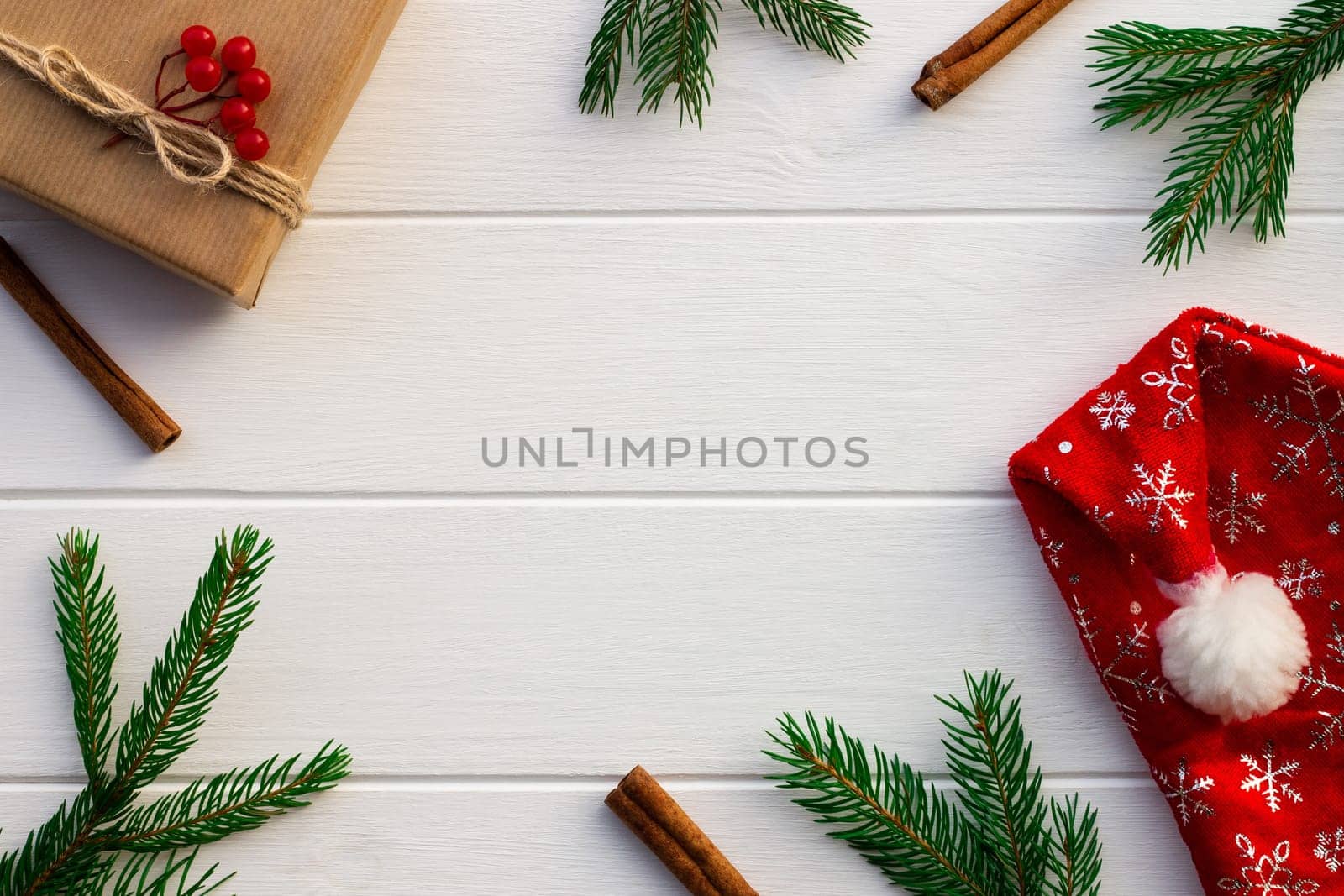 Gift with green branches of a Christmas tree, red berries, cones, cinnamon sticks on a background of white boards. Flat lay. Copy space.