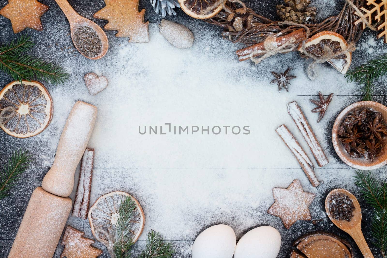 Flour New Year background. Christmas tree branches, gingerbread cookies, spices and baking supplies on black wood background. Christmas, New Year greeting card