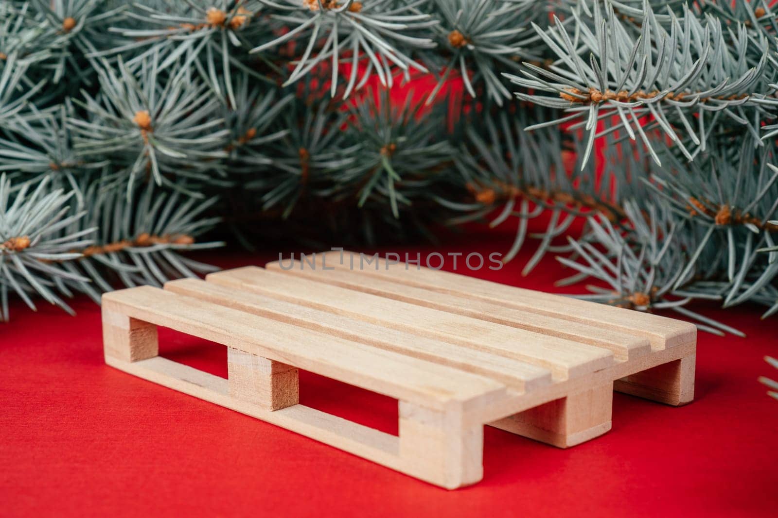 Happy New Year 2022. Wooden podium in form of pallet on red surface with Christmas tree branches. Podium, pedestal or stage. Mockup for products on red background. Merry Christmas.