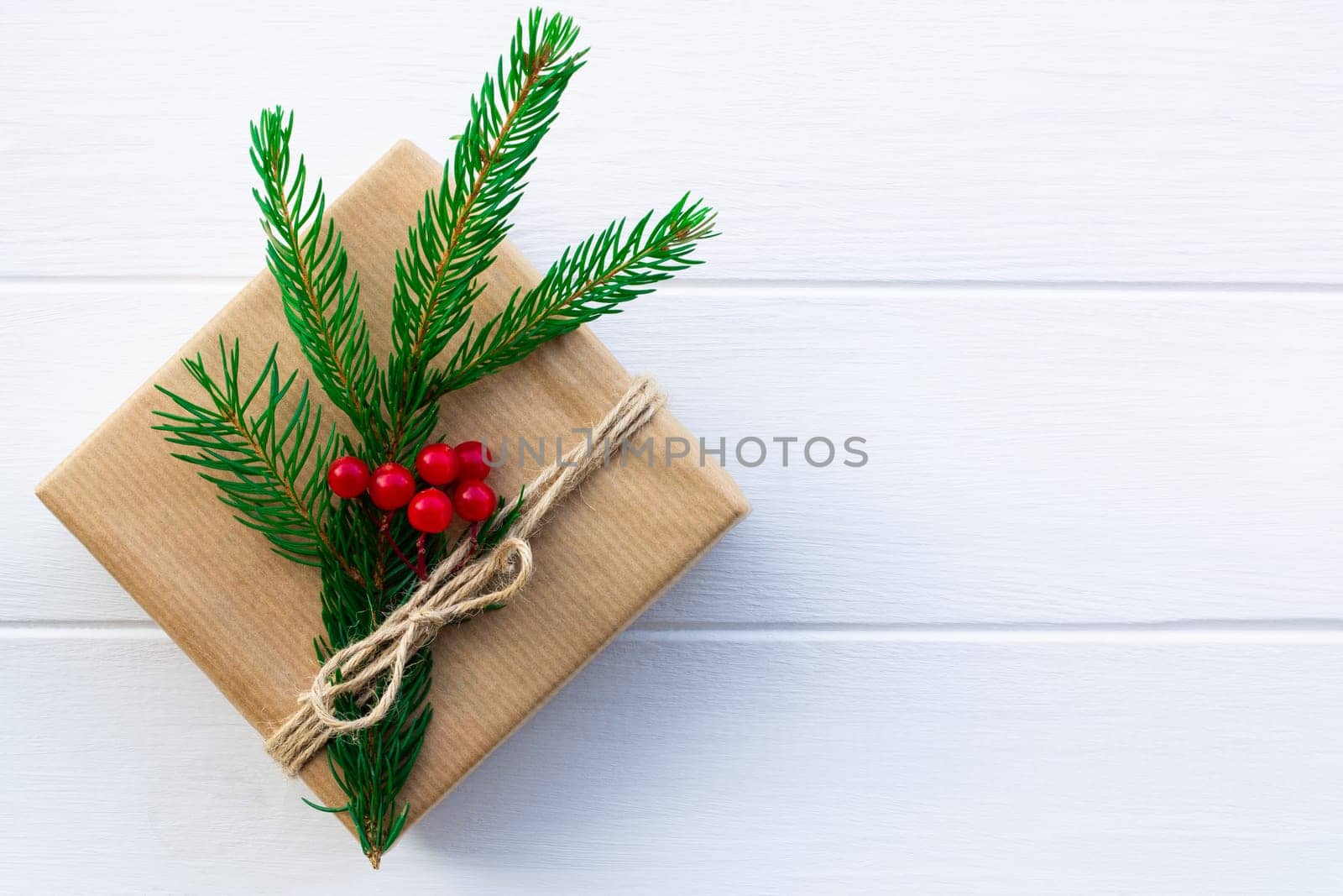 Gift with green branches of a Christmas tree and red berries on a background of white boards. Flat lay. Copy space