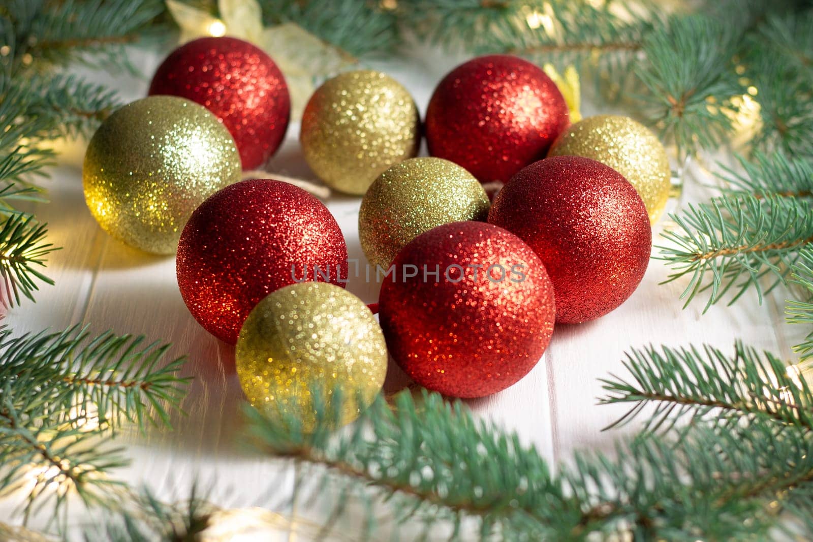Green branches of a Christmas tree with LED light bulbs, garland and shiny balls on a white wooden background. Merry Christmas and Happy New Year concept