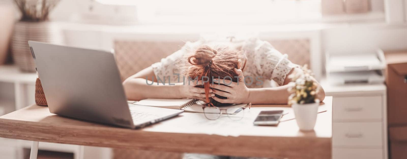 Tired woman putting her head on her hands on the desk in the office. Concept of overworked.