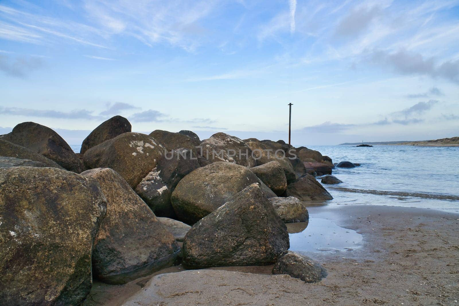Stone groyne juts out into the water off the coast in Denmark. Sunny day. Landscape photo by the sea