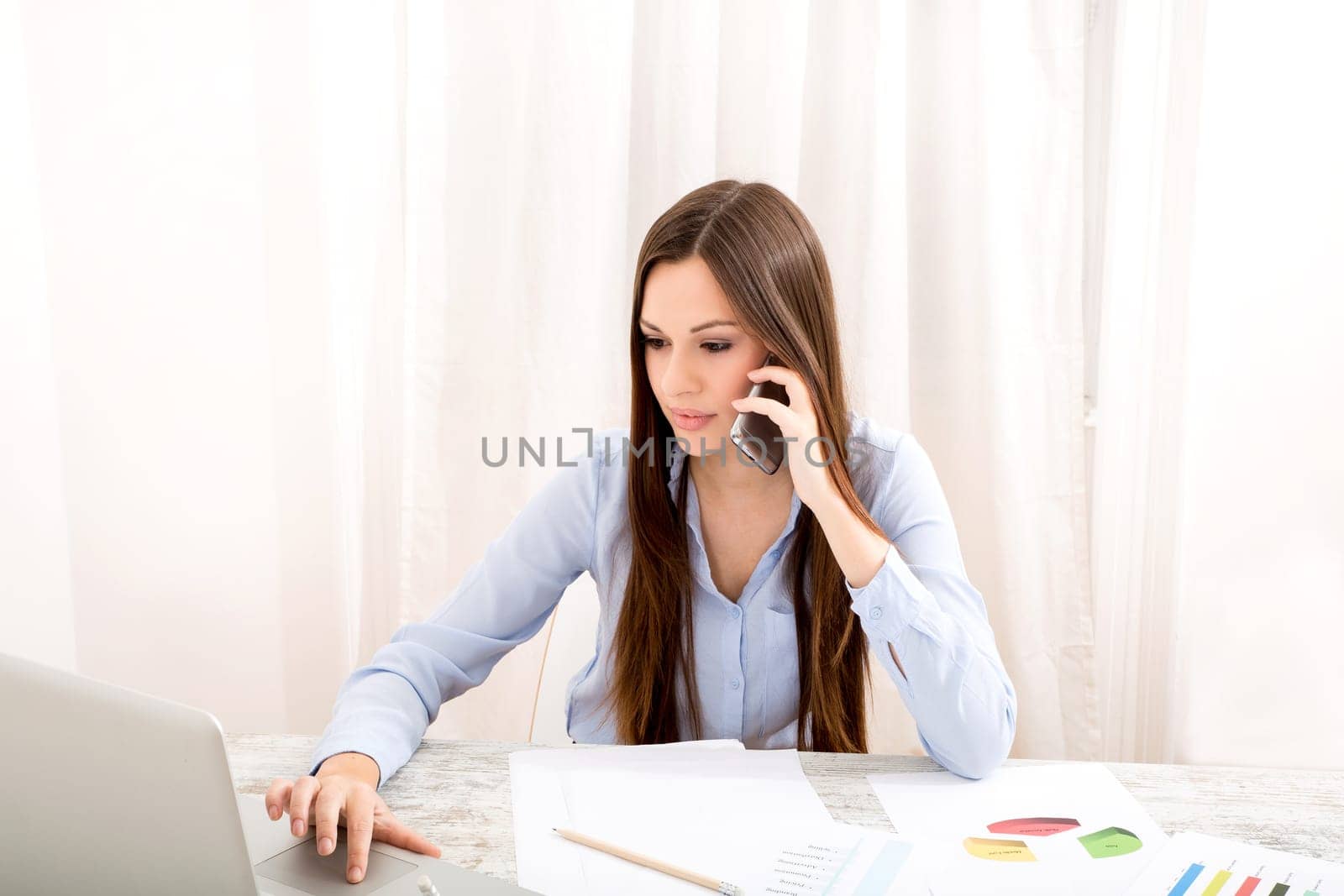 Businesswoman working at the office with the laptop and some documents and talking by the phone.