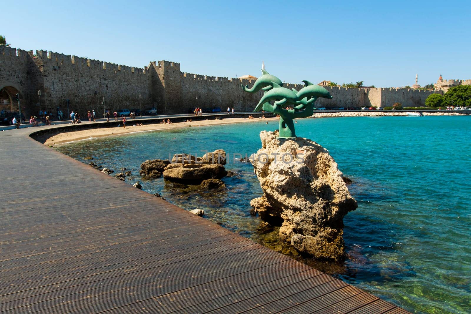 View of the dock of the pier of Rhodes with sculpture in the foreground and the city walls' in the background