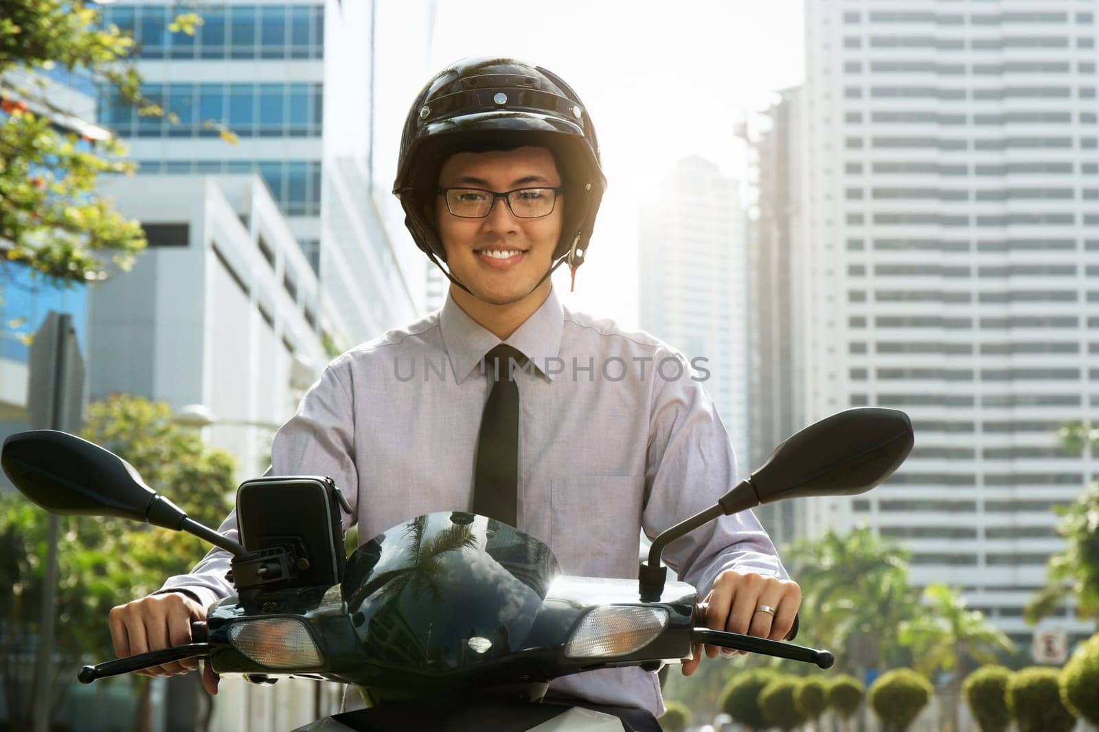 Young asian businessman commuting to job. The man rides a motorcycle scooter with white helmet and smiles at camera