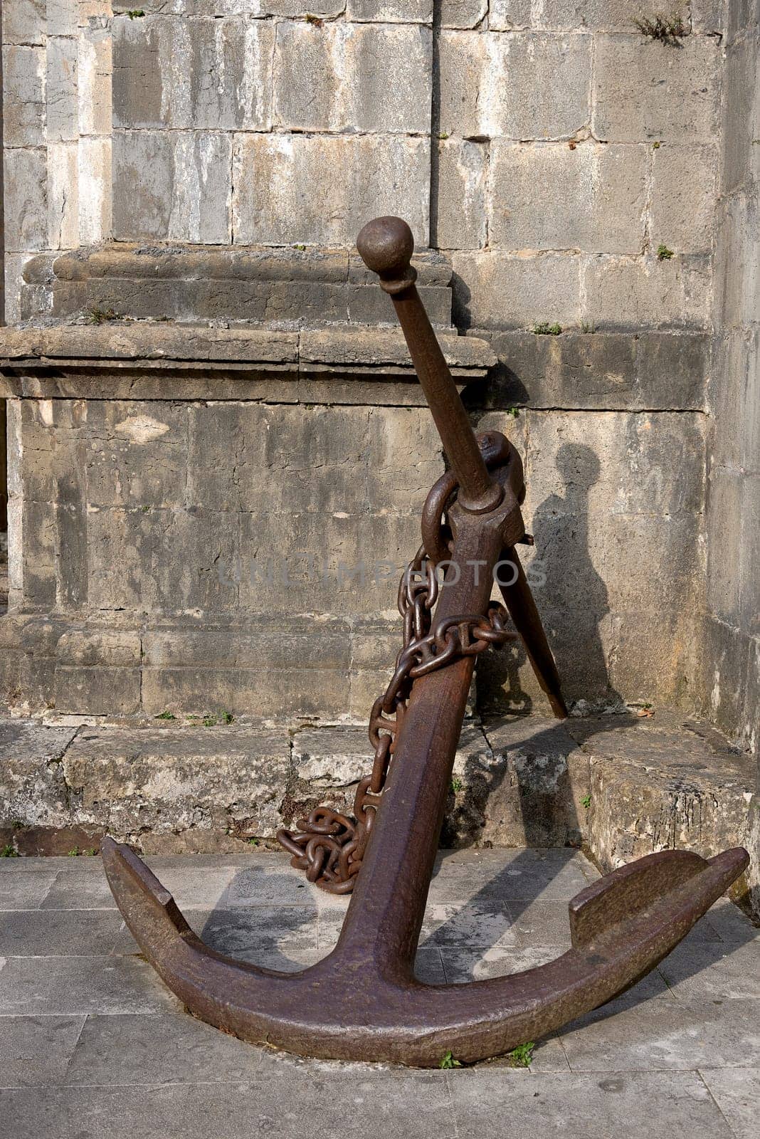 Large antique ship anchor leaning against the wall. stone wall, masonry, texture, bronze colour, shadows, etc.