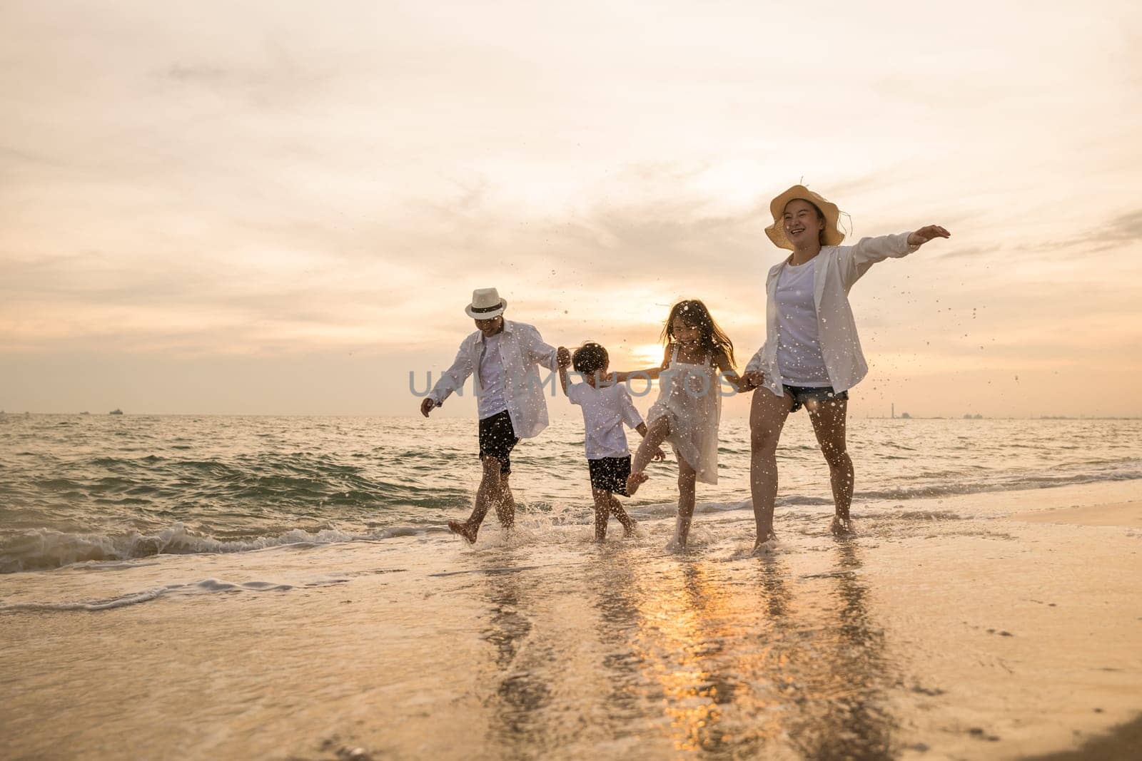 Tropical summer vacations, Happy family having fun running on a sandy beach at sunset time, People of father, mother, children son and daughter family of four holding hands together walking on beach