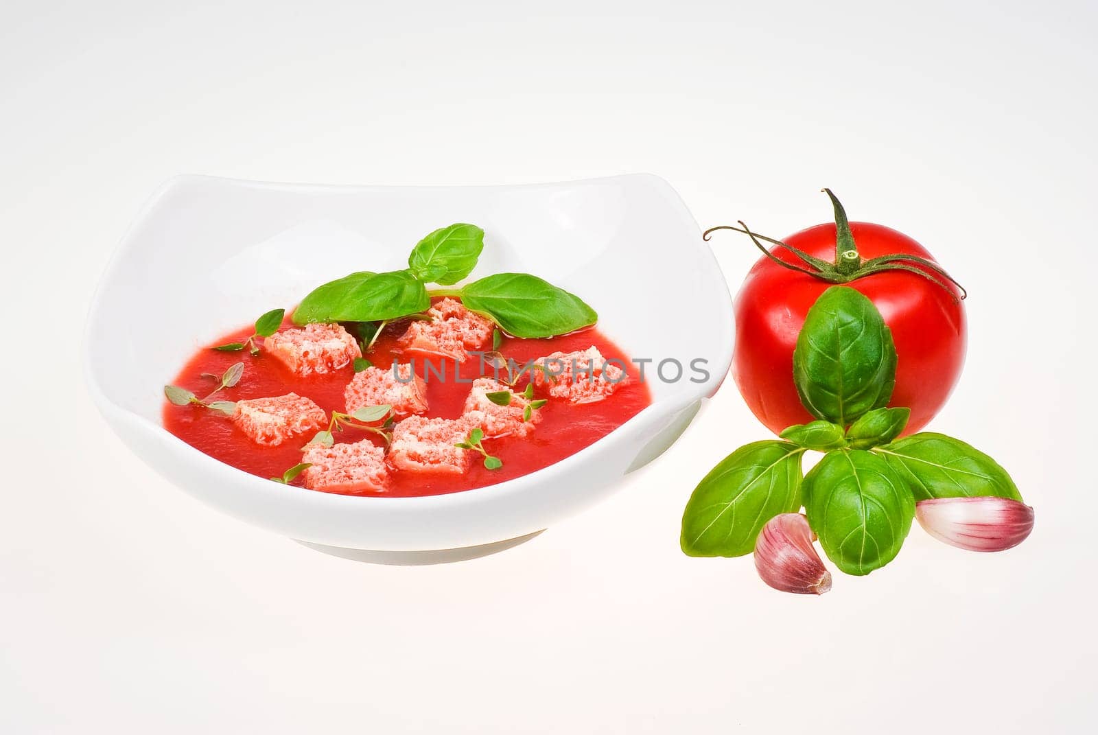 Bowl of tomato soup with tomato, basil and garlic over  white background