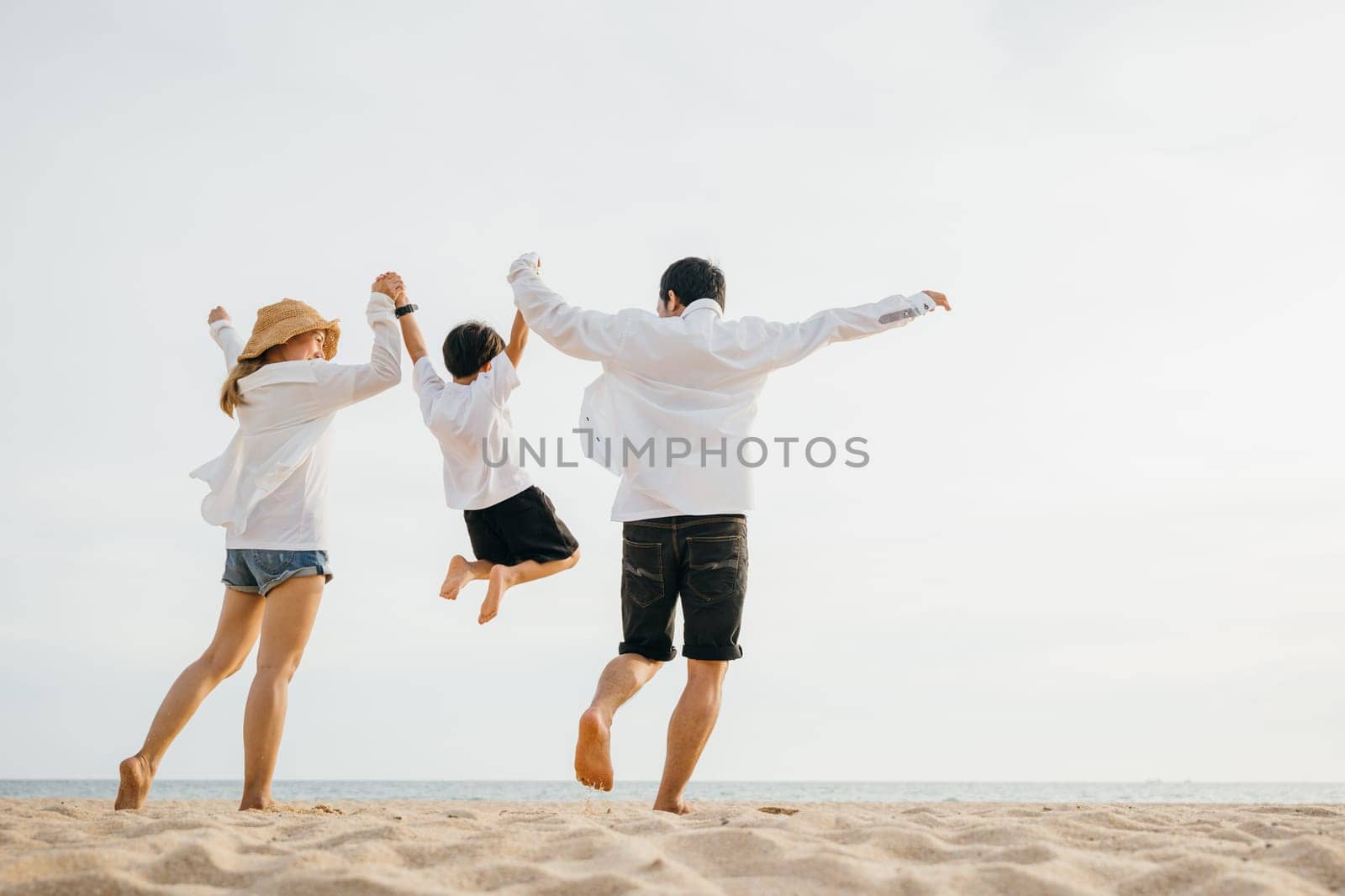 Family outdoor activities, Back family mother, father and son holding hands and jumping in air at dawn time, Happy Asian family people have fun together on beach on holiday summer vacation travel