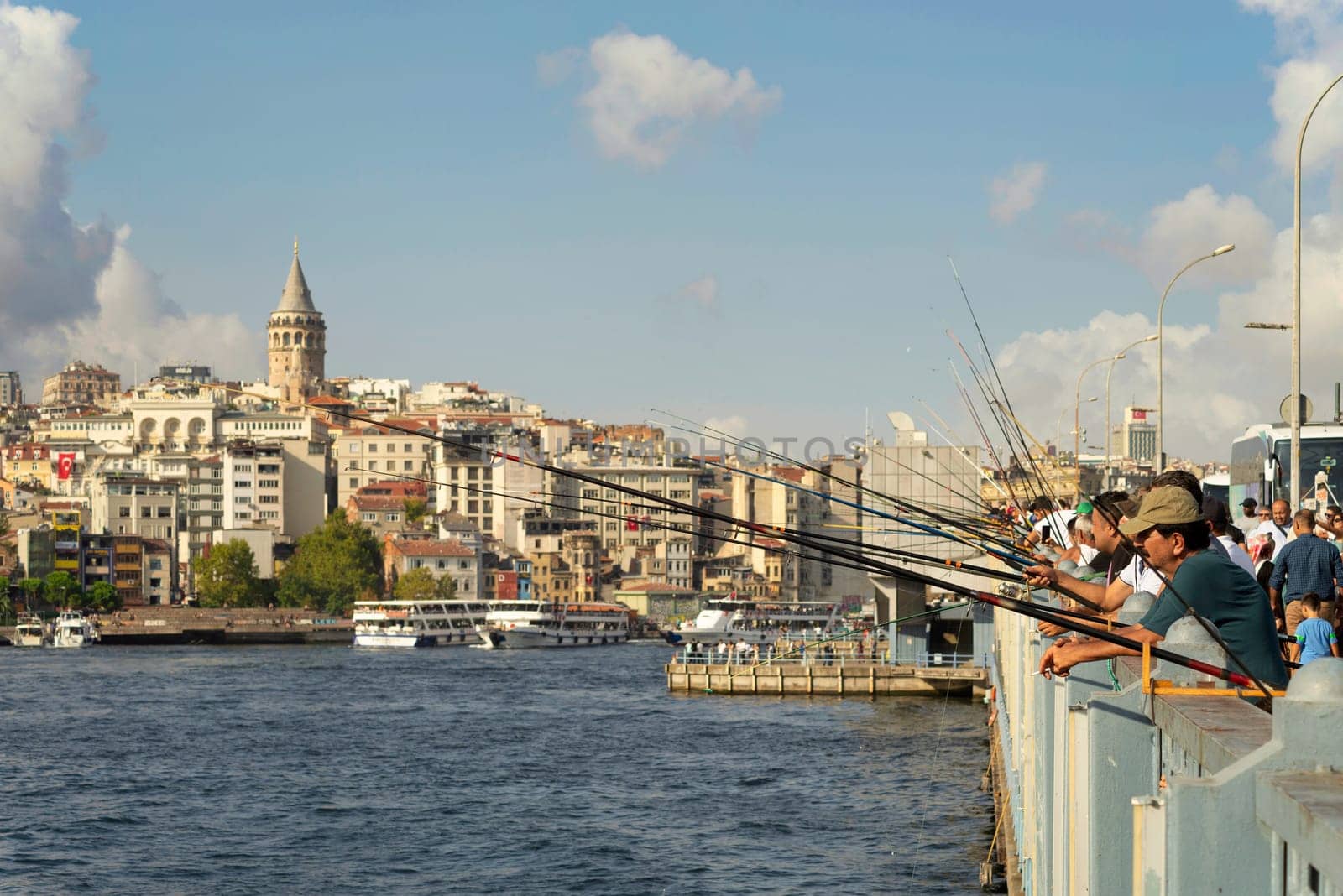 Istanbul, Turkey - August 30, 2022: Local citizens fishing at Golden Horn on Galata Bridge before sunset with Skyline of Istanbul in the background, including Galata Tower, at Eminonu district