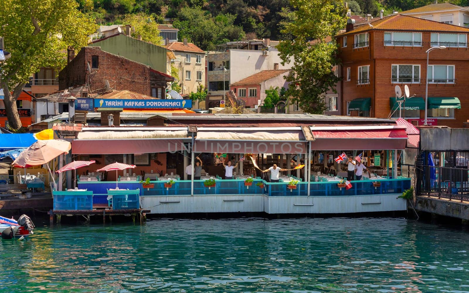 Istanbul, Turkey - August 29, 2022: Shot from ferry boat of floating restaurant staff waving flags and dance to welcome visitors of Anadolu Kavagi neighborhood, at the Asian side of Bosphorus Strait