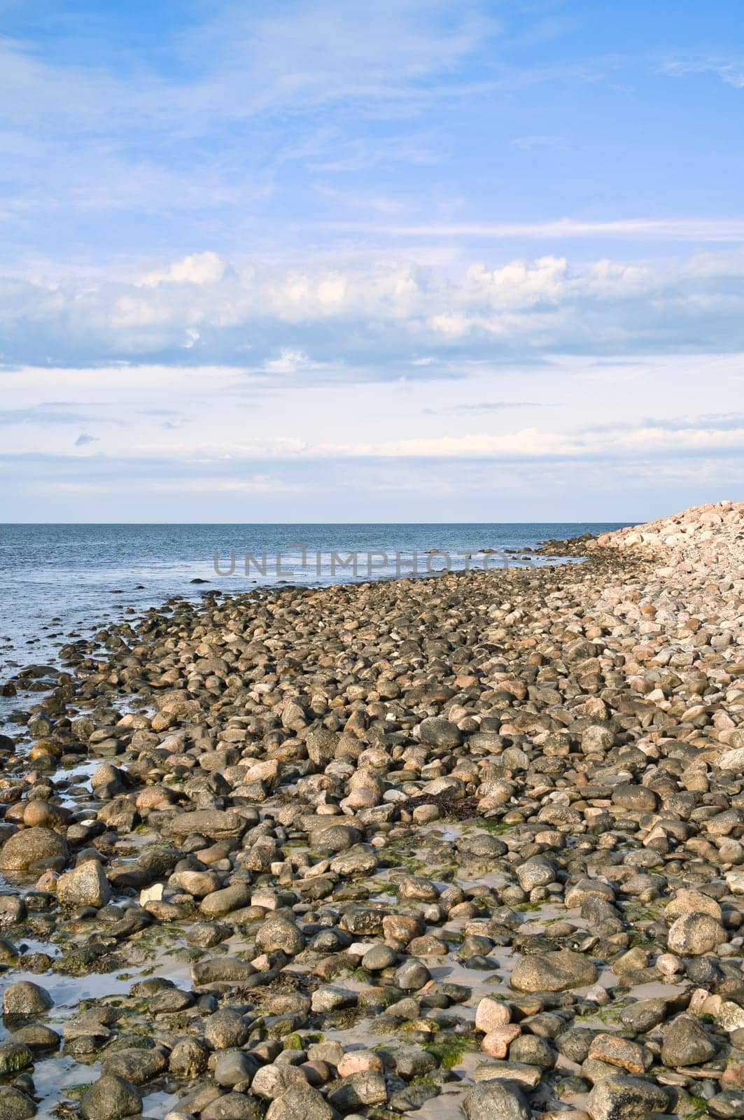 Stone beach by the sea. Danish coast on a sunny day with clouds in the sky. Landscape shot at the water