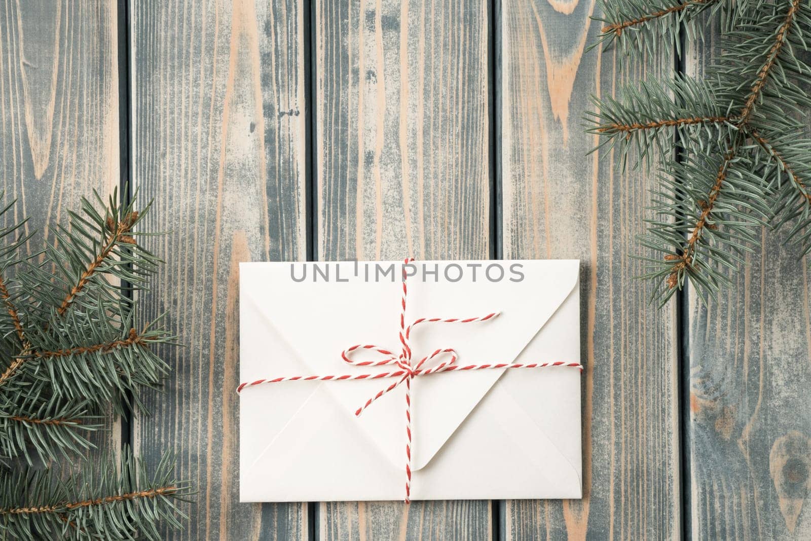 White envelope on on gray wooden background with branches of Christmas tree. New year envelope tied with cord with bow. Top view