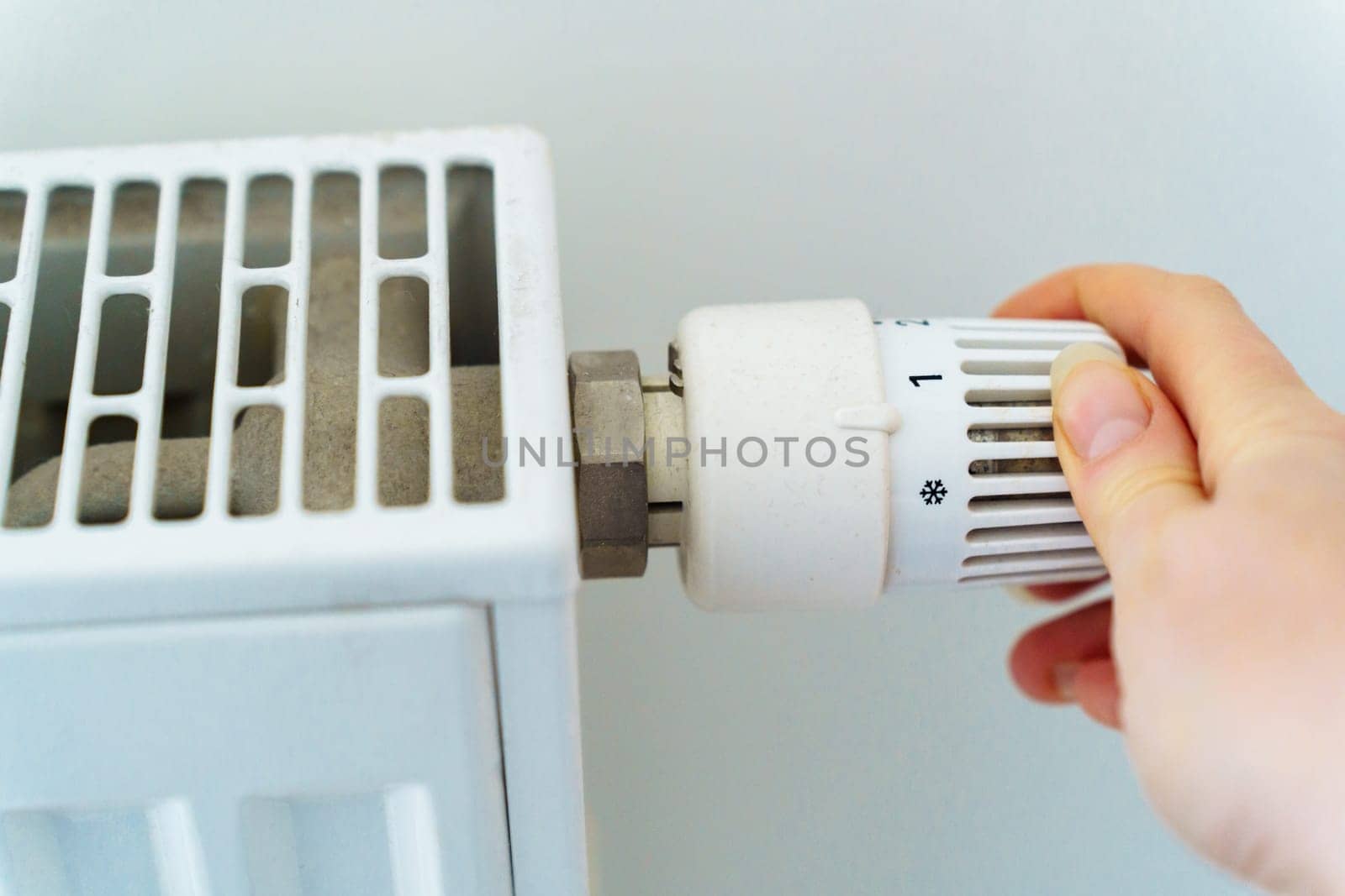 A woman's hand switches the radiator heating regulator to a minimum to save heat energy due to rising prices for nuts and utilities.