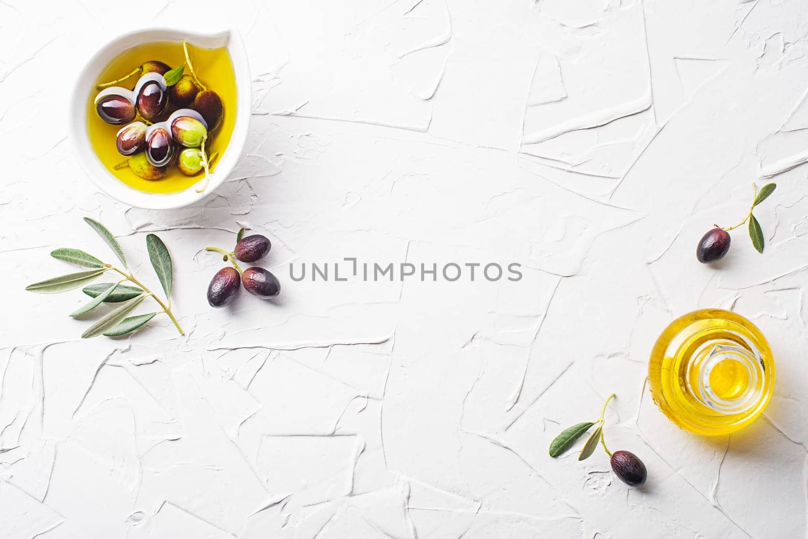 Olive oil in bowl with fresh olives fruit and olive branch on white background close up