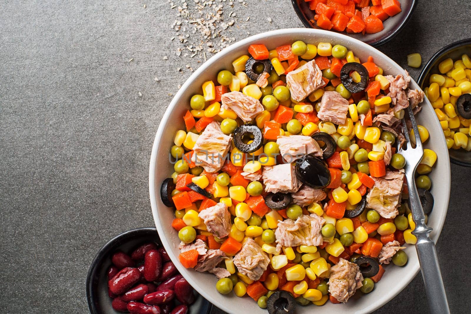 Healthy mixed tuna salad with corns, carrots, peas, beans and olives on grey table background. Mexican corn salad.