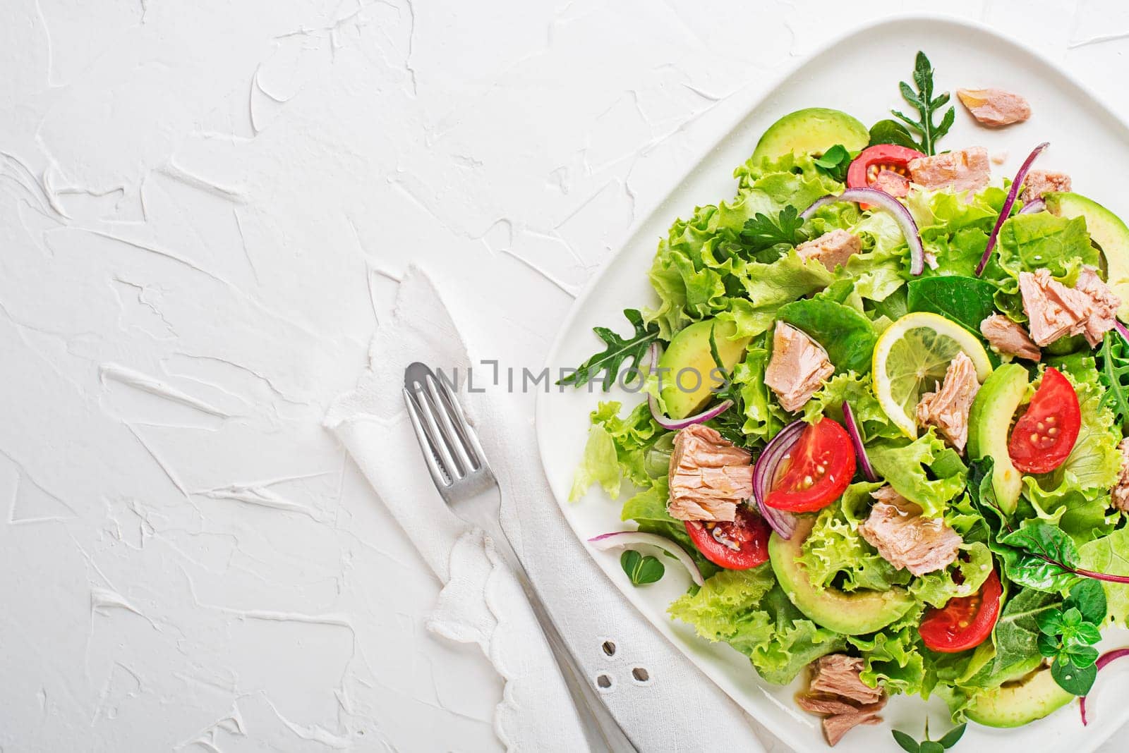 Fresh green leafy salad with tuna avocado and tomato on white table background. Concept for a tasty and healthy meal