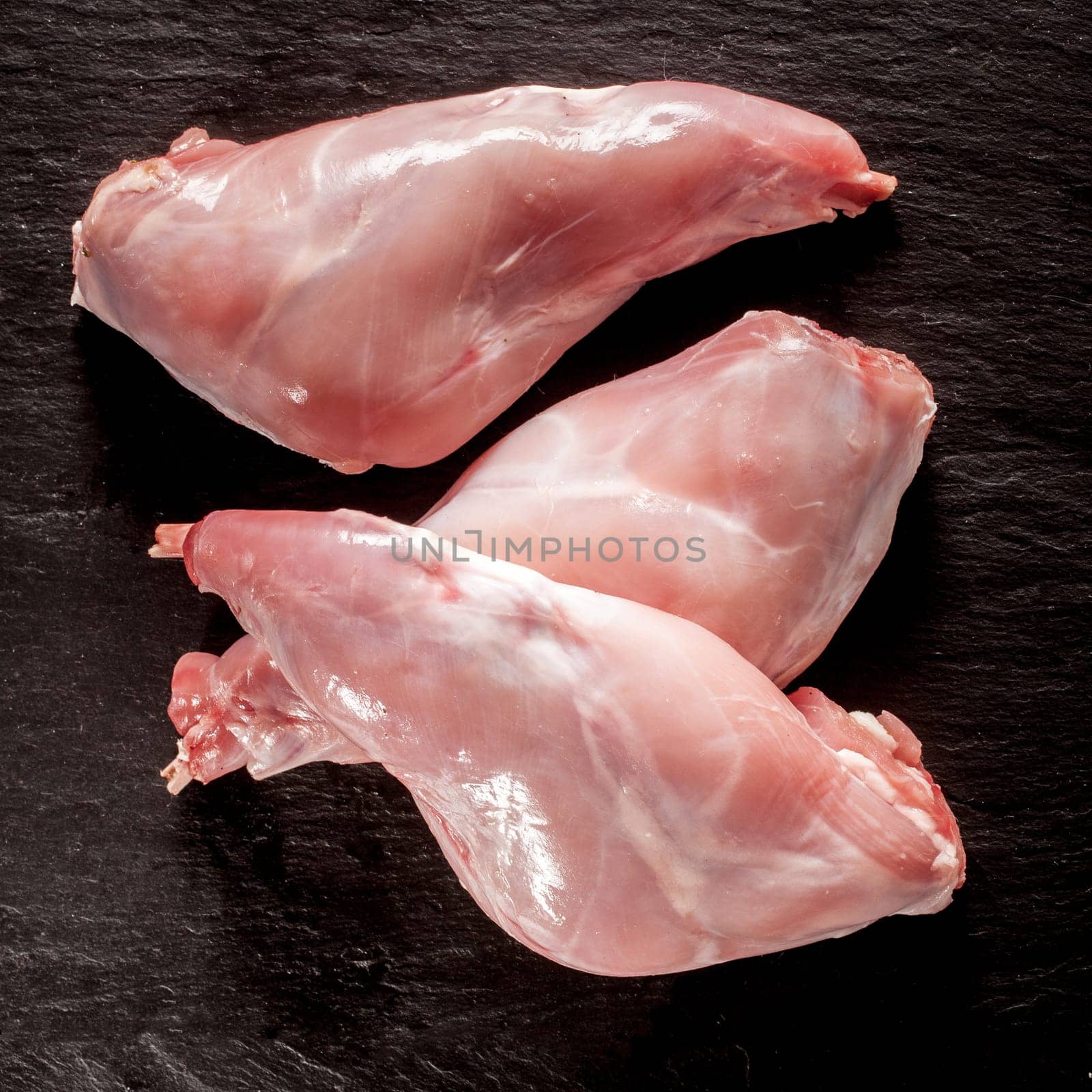Uncooked fresh wild rabbit or hare haunches ready for roasting or grilling for tasty venison cuisine on a textured black background