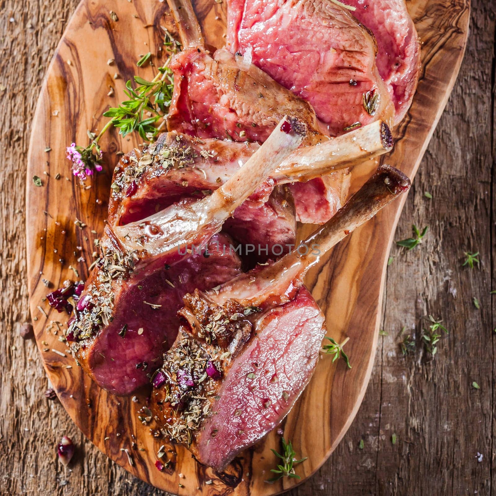 High Angle View of Rare Rectangle Lamb Chops Sliced and Seasoned with Fresh Herbs on Wooden Cutting Board