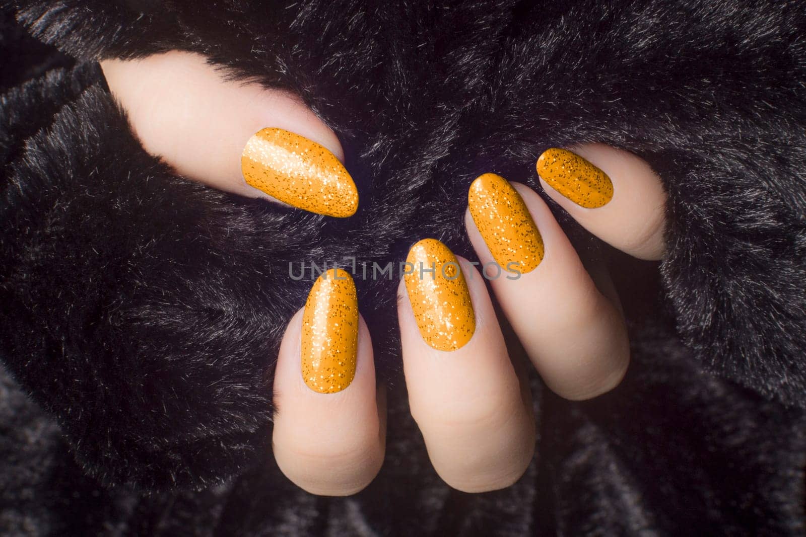 Female hand with glittered orange nails is holding black fur, manicure and nail care concept.