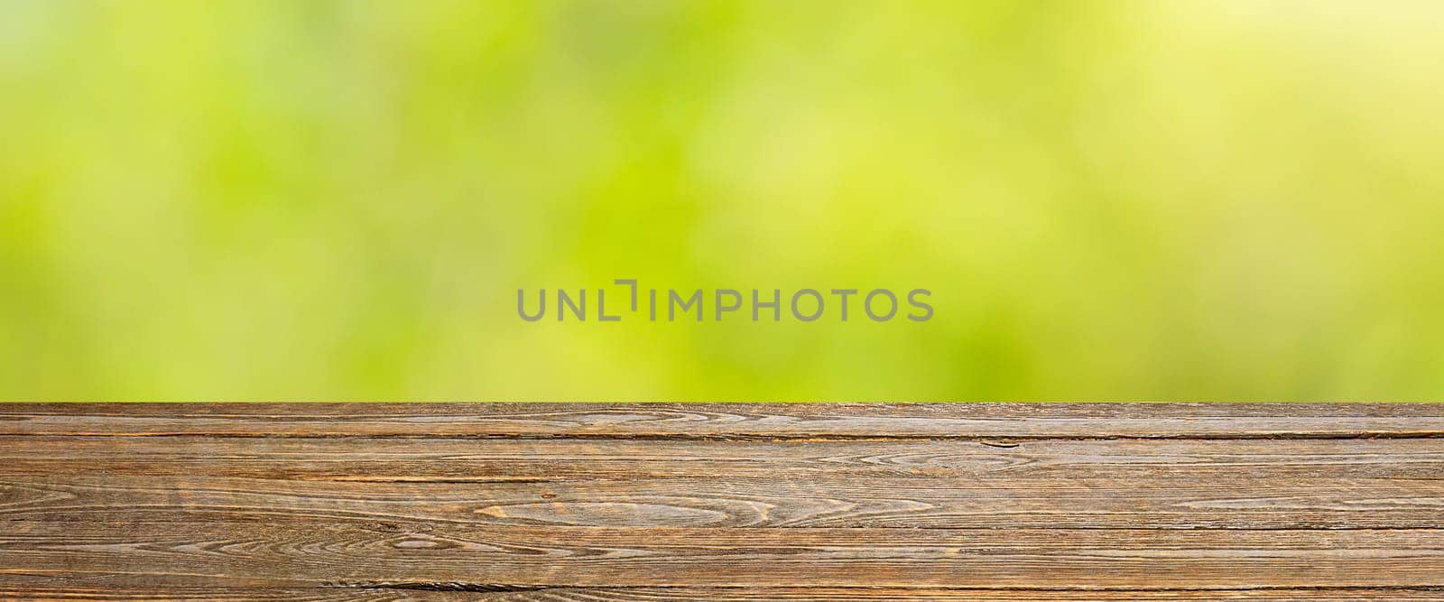 Background with blurred green leaves and empty wooden planks in the foreground. For product demonstrations, free space, layout, mockup, perspective board, background board.