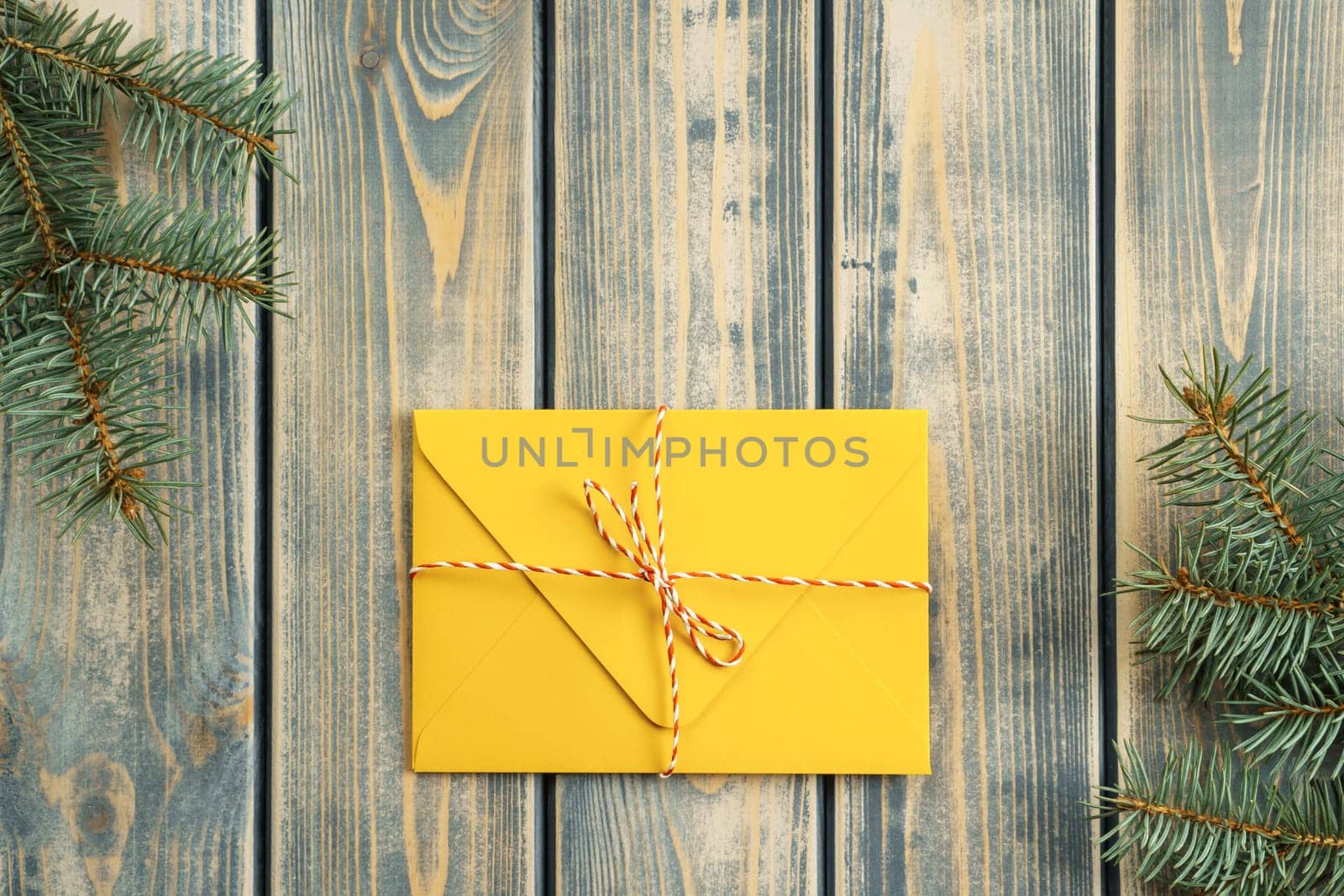 Yellow envelope on gray wooden background with branches of Christmas tree. New year envelope tied with cord with bow. Top view