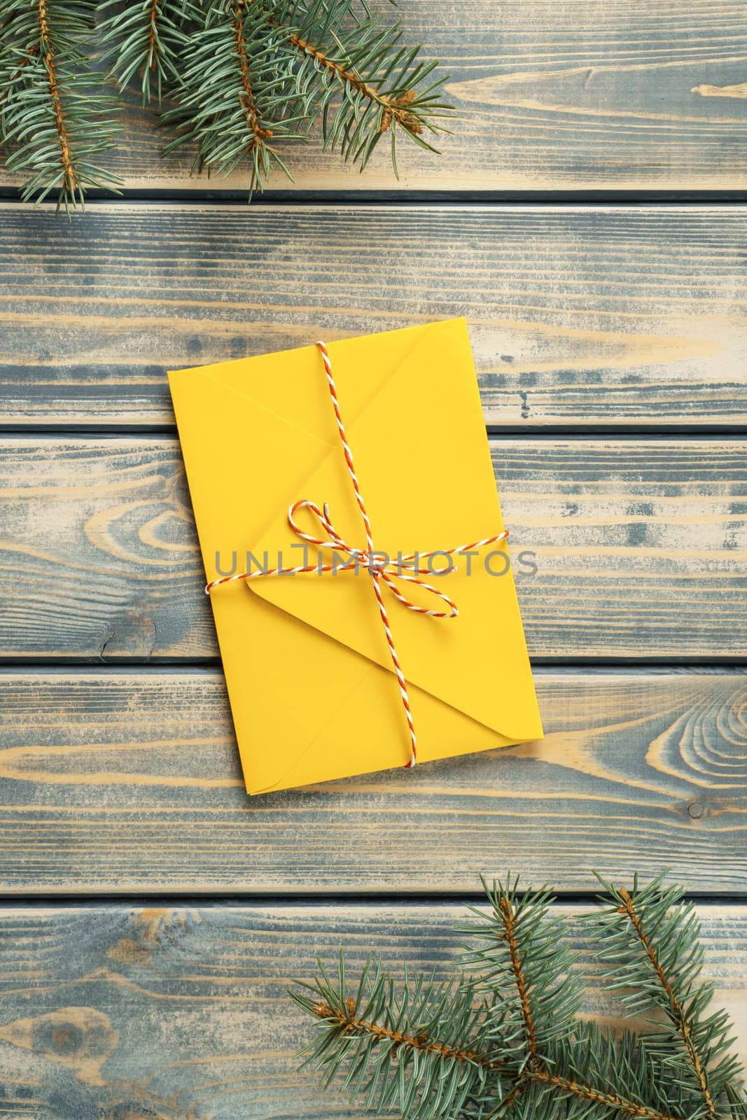 Yellow envelope on gray wooden background with branches of Christmas tree. New year envelope tied with cord with bow. Top view. Vertical