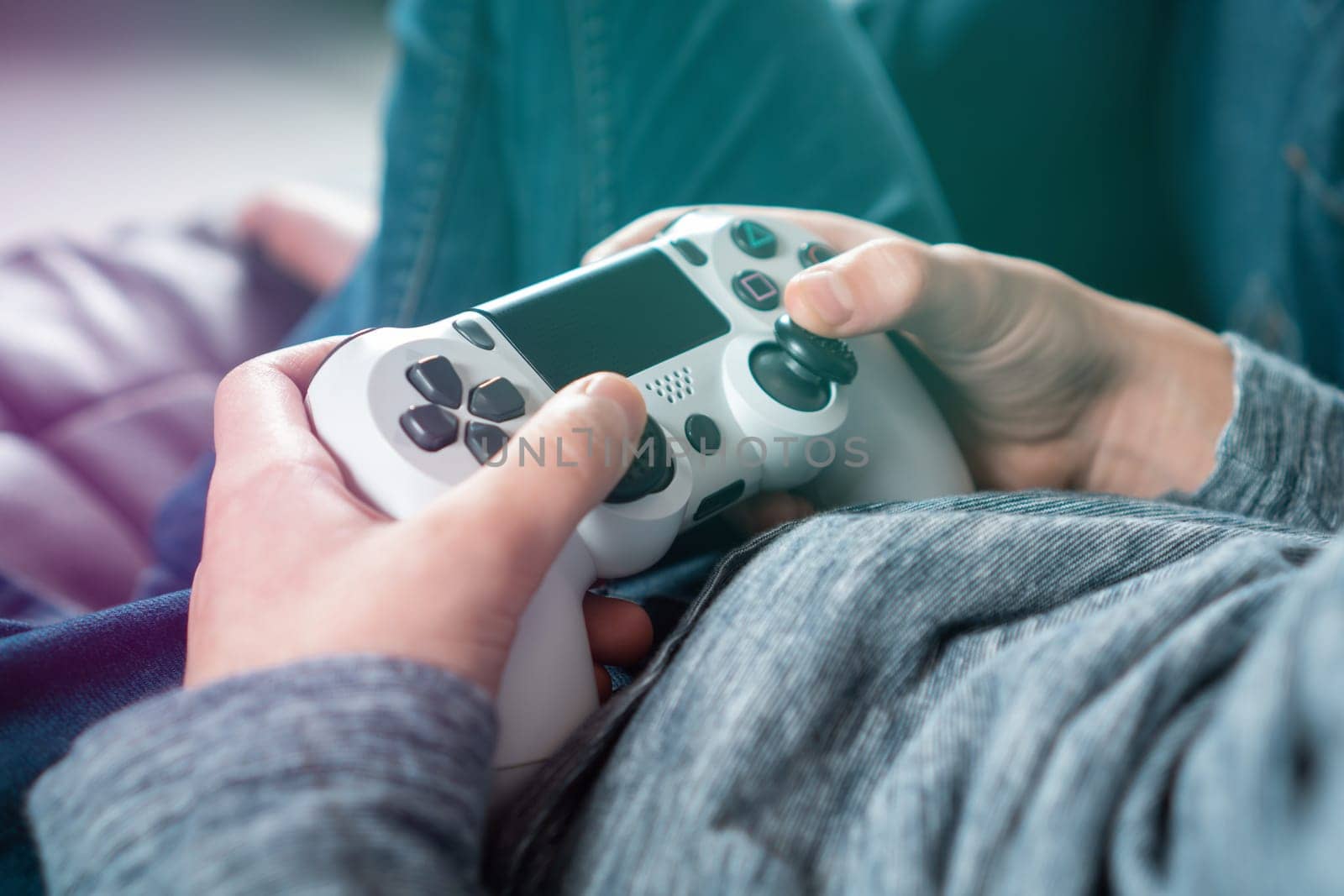 Cropped photo of teenage boy sitting at home, holding white gaming controller joystick gamepad, playing videogames on console station. Hobby, free time, gaming, entertainment, leisure. Soft focus.